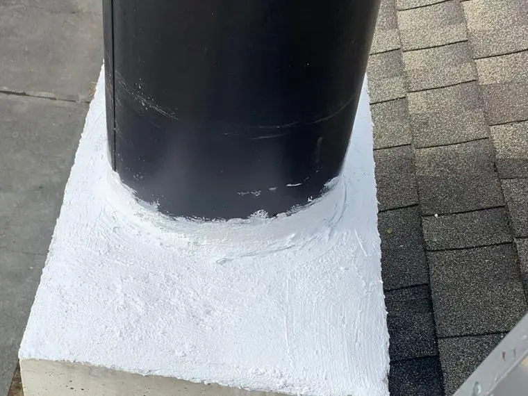 A black metal flue pipe rising from a white-coated concrete crown on a brick chimney