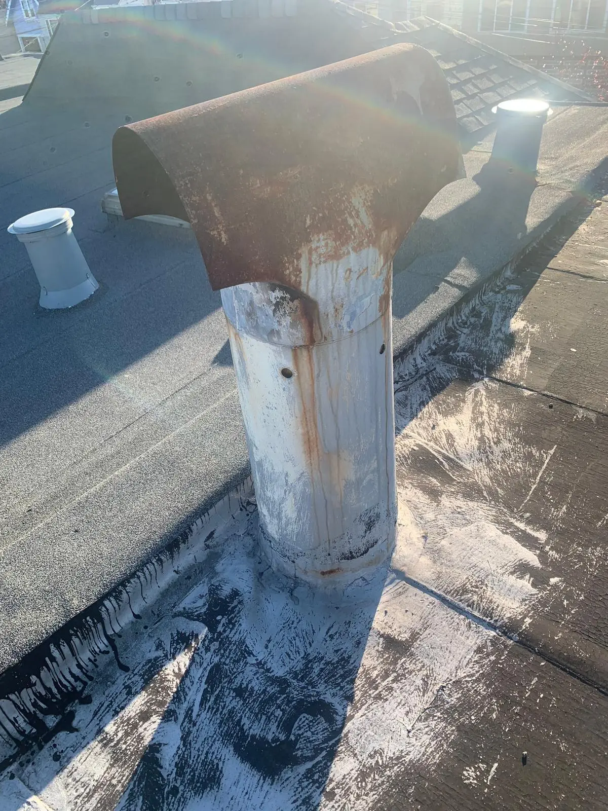 A rusted metal flue pipe with a corroded hood rising from a flat roof